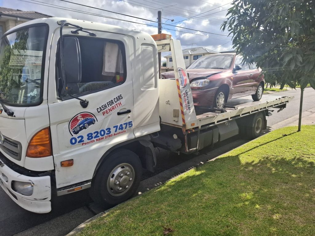 Red Daewoo Lanos with front-end damage on the Cash For Cars Penrith tilt-tray truck