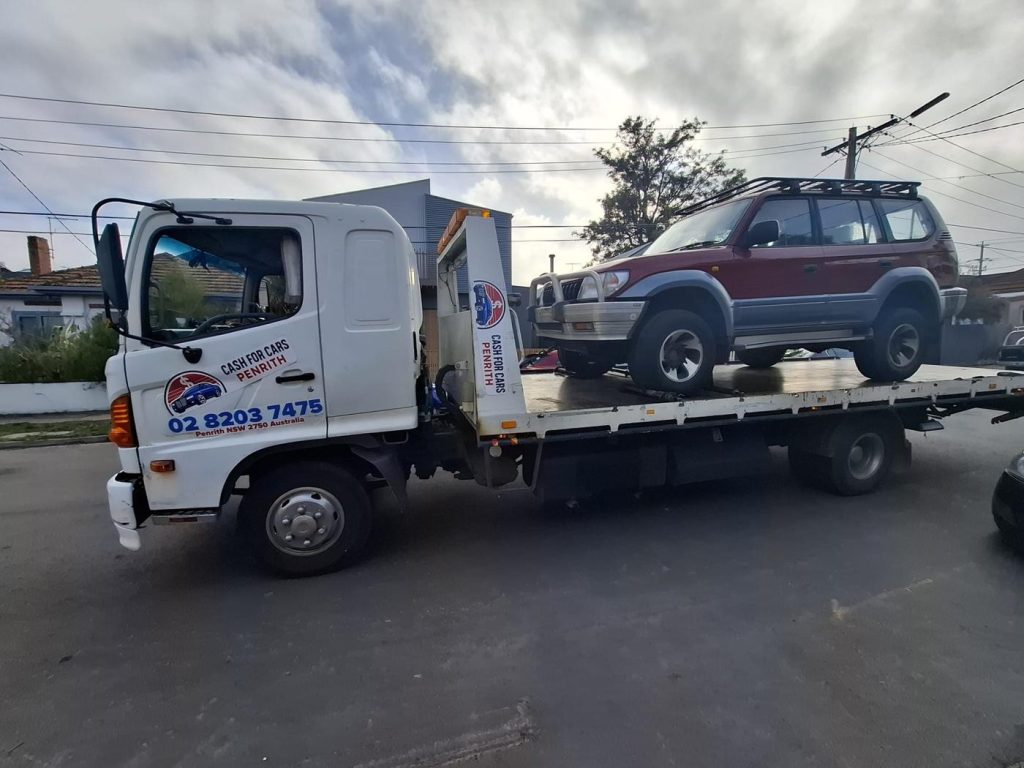 Red Toyota LandCruiser Prado 4WD with roof rack on the Cash For Cars Penrith tilt-tray truck